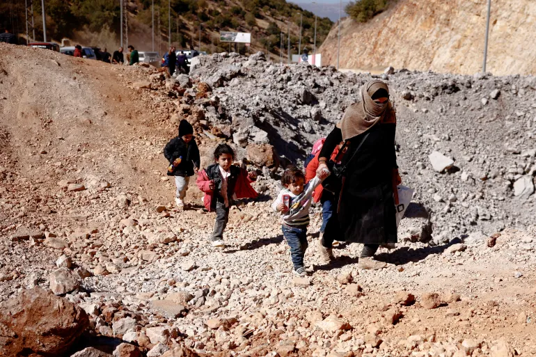 A woman walks with children while crossing from Lebanon into Syria on foot at the Masnaa border crossing, after an Israeli strike, in Al Masnaa