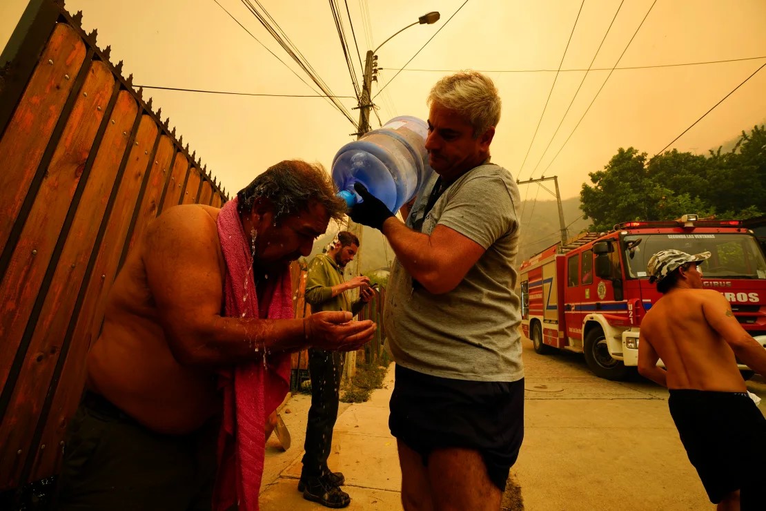 photo: A man helps a fellow resident cool down with bottled water as forest fires burn nearby. 