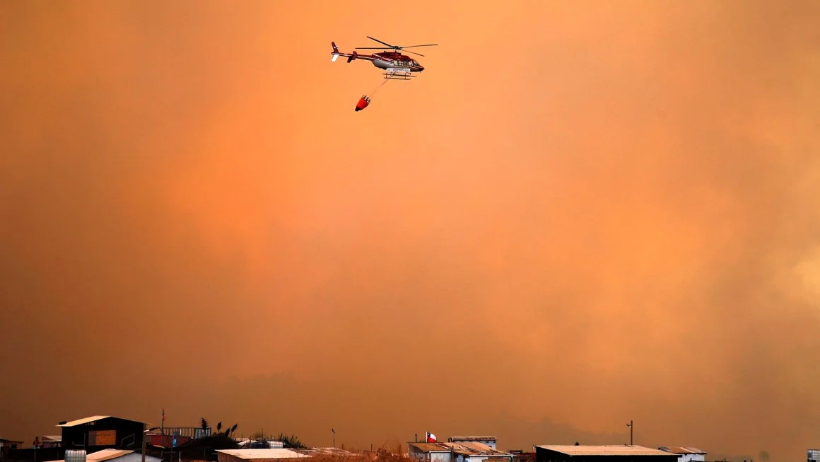 photo: A helicopter works on the zone of a forest fire in the hills in Quilpe comune, Valparaiso region, Chile.